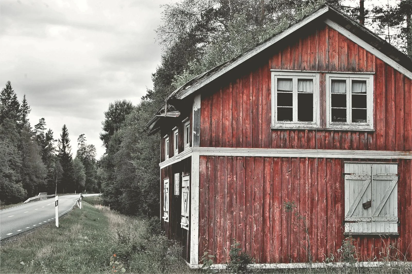 Tühjaks jäänud punane puumaja metsatee ääres, värv koorub ja rohi ulatub seinani