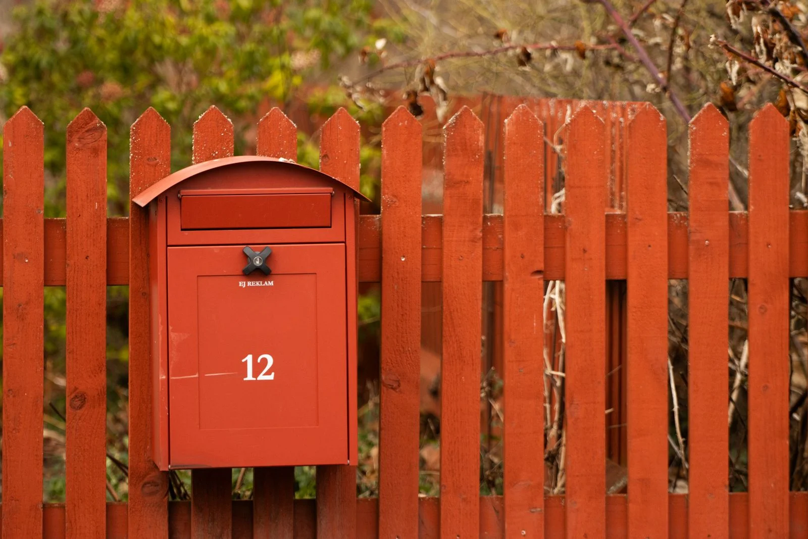 Punane postkast numbriga 12 samas toonis punase aiapiirde küljes, taga aiarohelus
