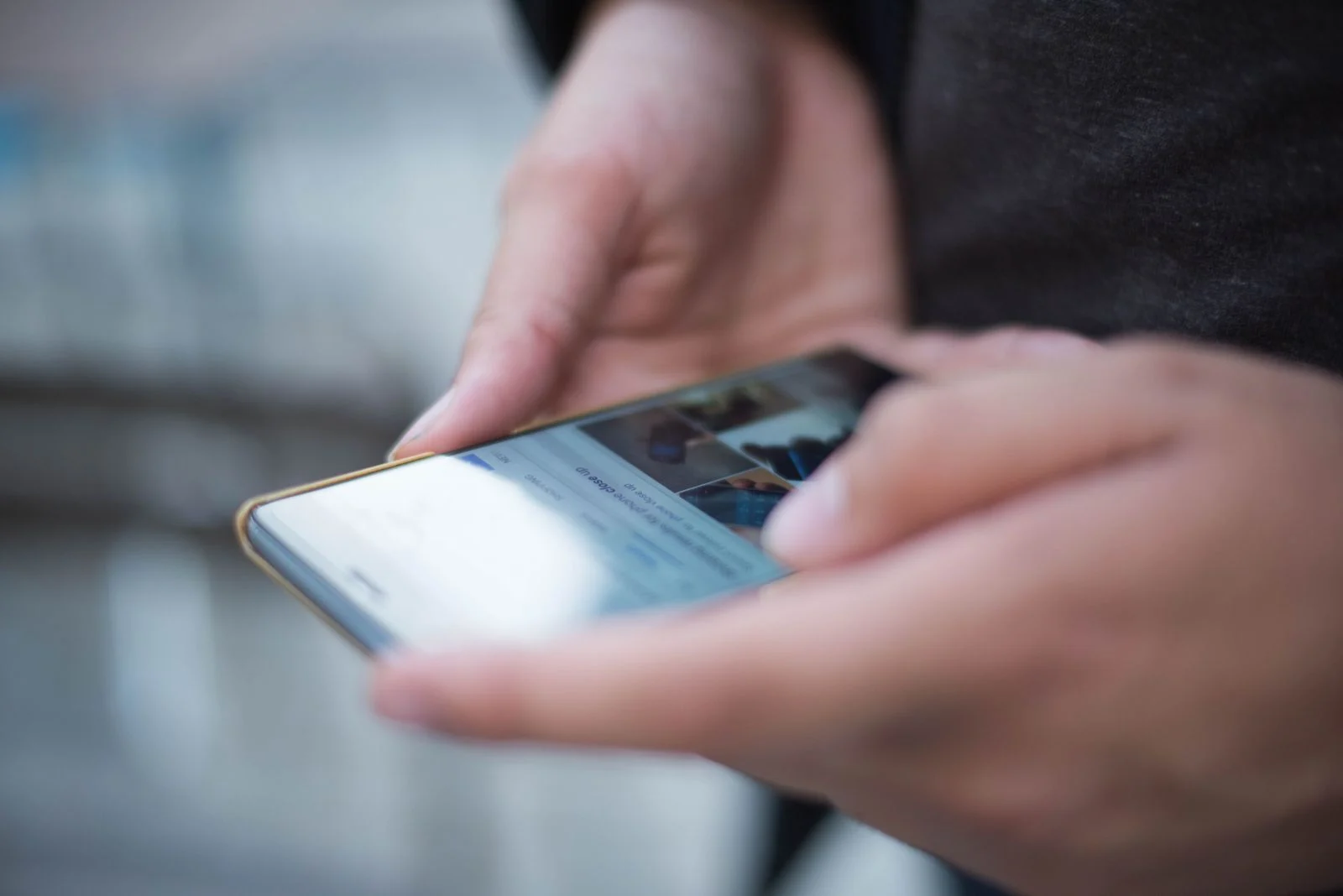 Kaks kätt hoiavad telefoni ja kerivad, ekraan on fookusest väljas, taga hägune tänav